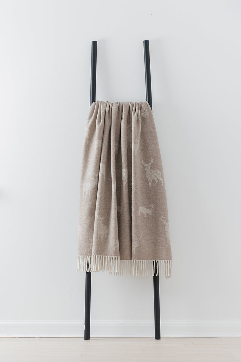 Beige blanket with stag pattern draped over a black ladder against a white background