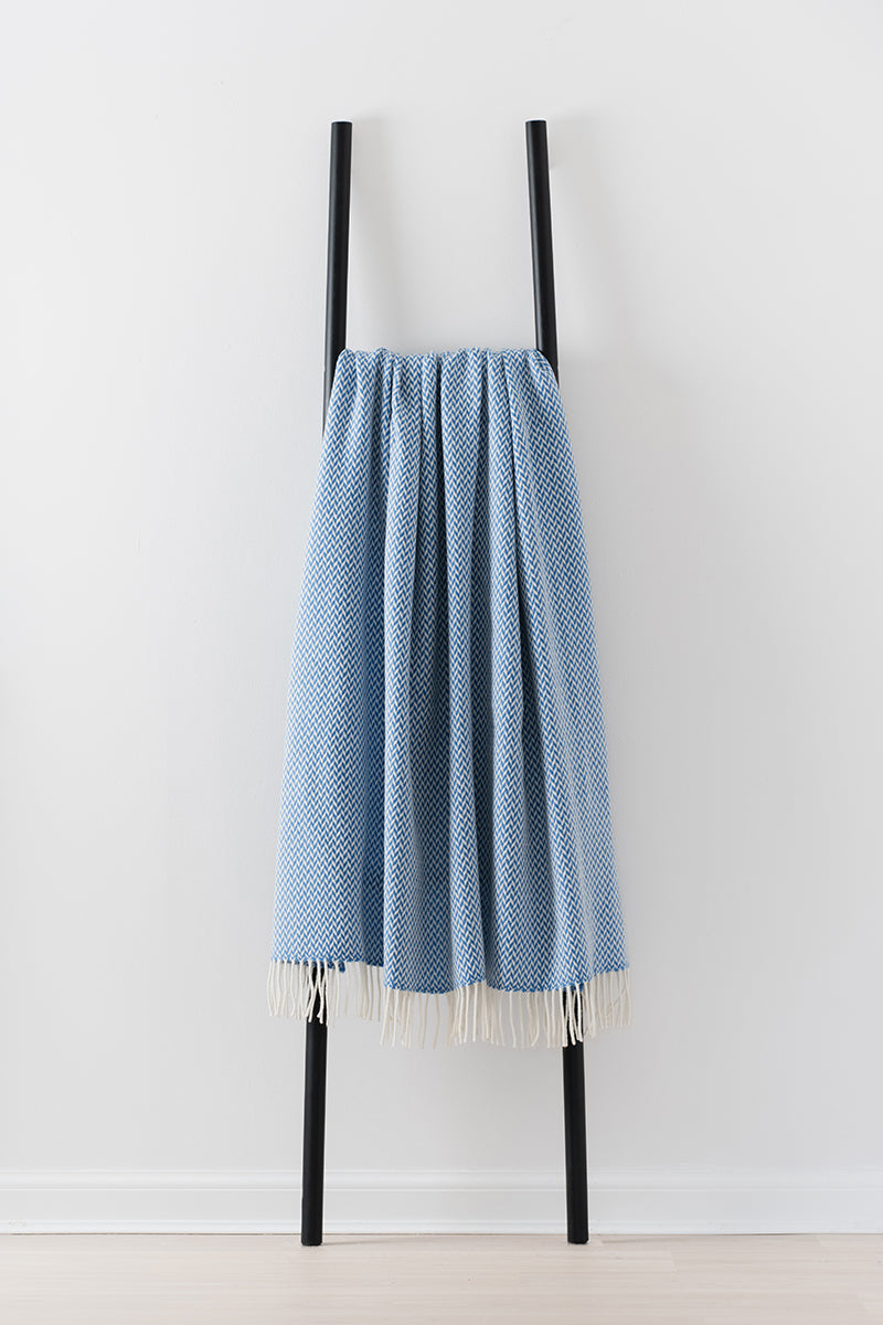 Remony balintyre blue throw - Blue herringbone blanket on a black metal ladder against a white background