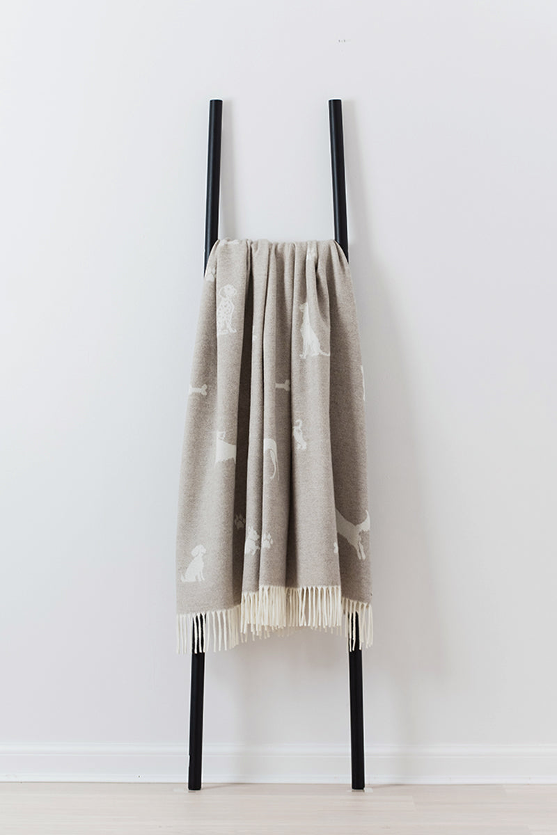 Beige multi dog pattern throwwith white patterns hanging on a black ladder against a white wall.