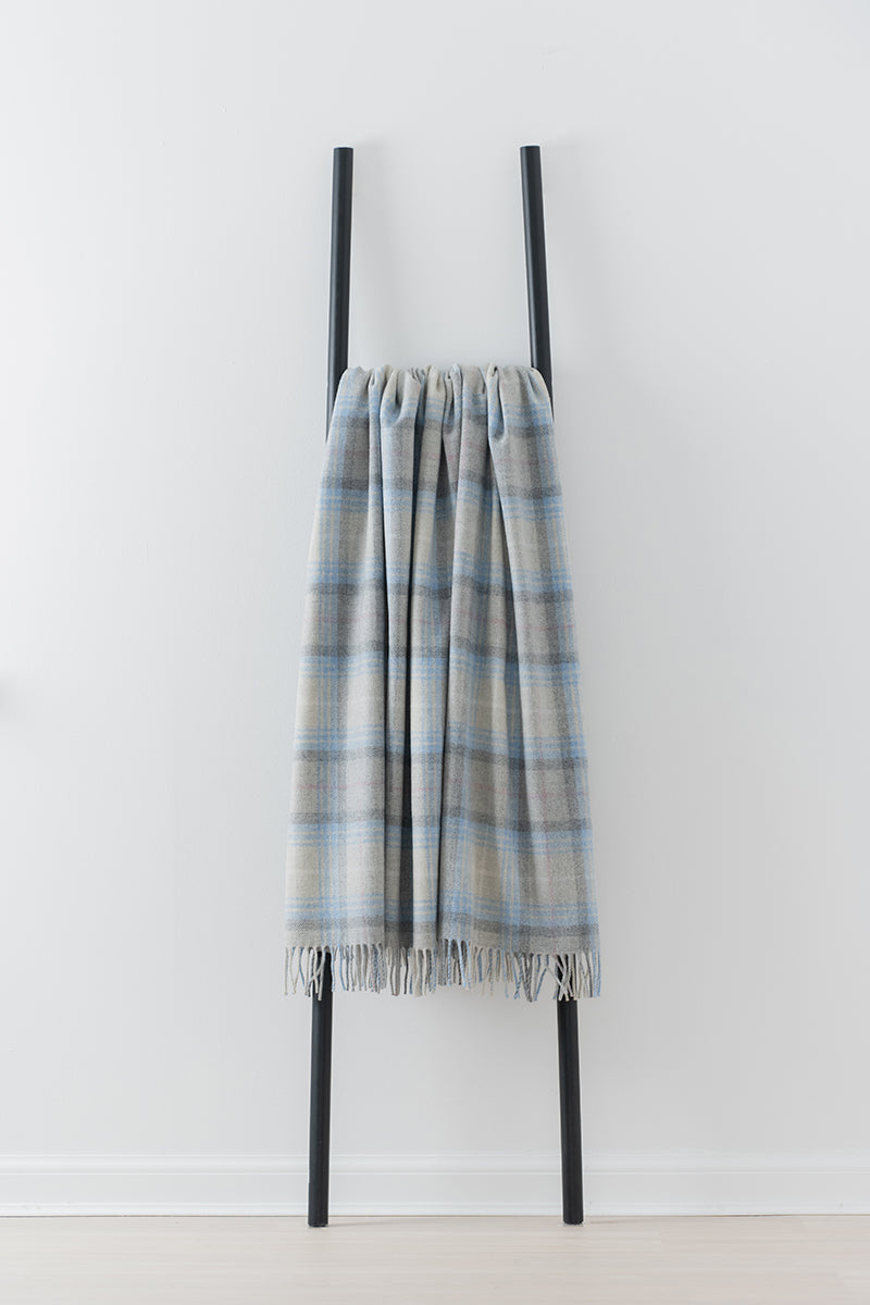 Remony lindores cornflower throw - Plaid blanket draped over a black metal ladder against a white background