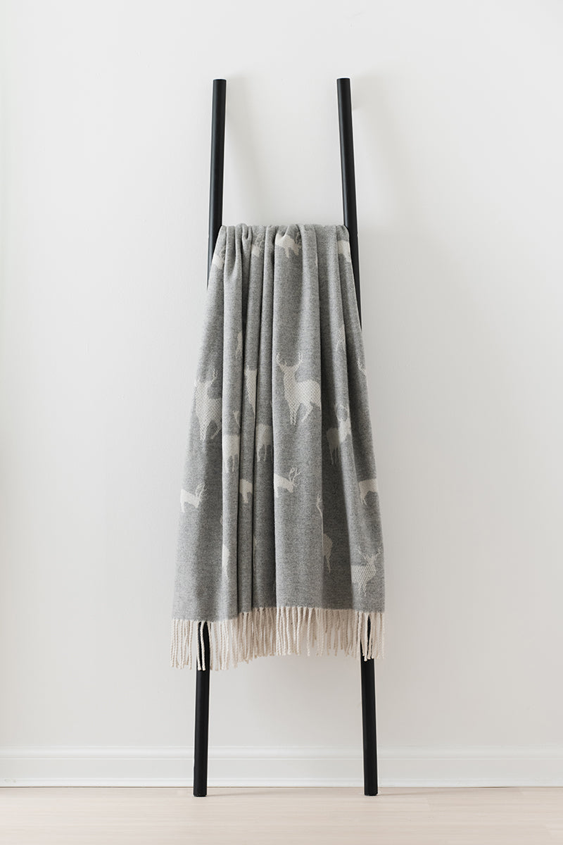 Remony nature stag gryy and white patterned throw with fringes on a black ladder against a white background