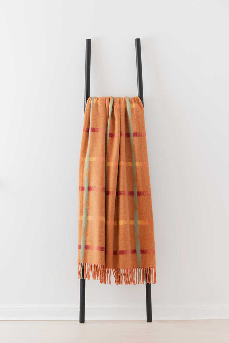 Remony maree spice throw - check blanket draped over a black metal ladder against a white background