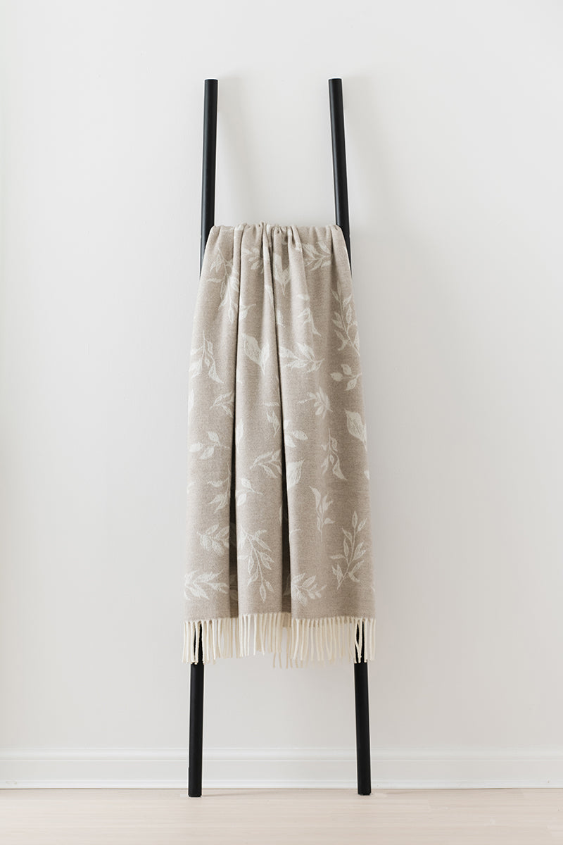Remony nature leaf oatmeal throw draped over a black ladder against a white wall.