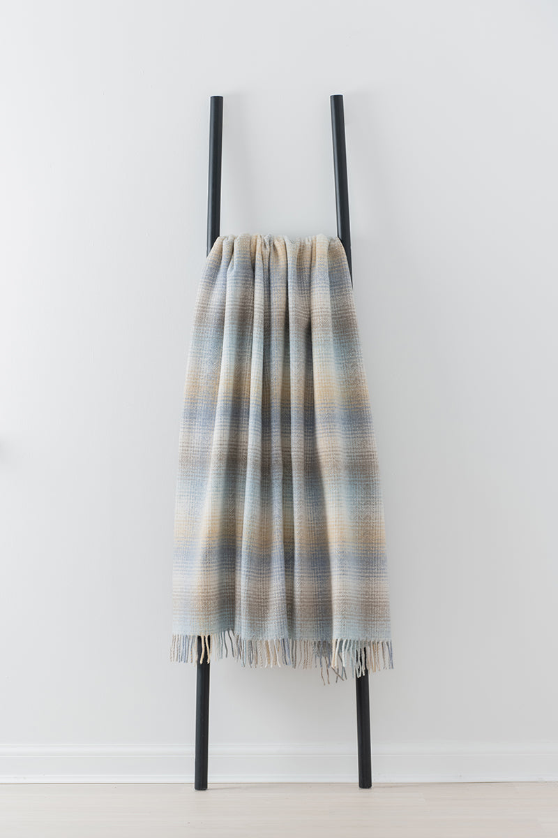 Remony Lunan Shore Throw - Plaid blanket draped over a black metal ladder against a white background