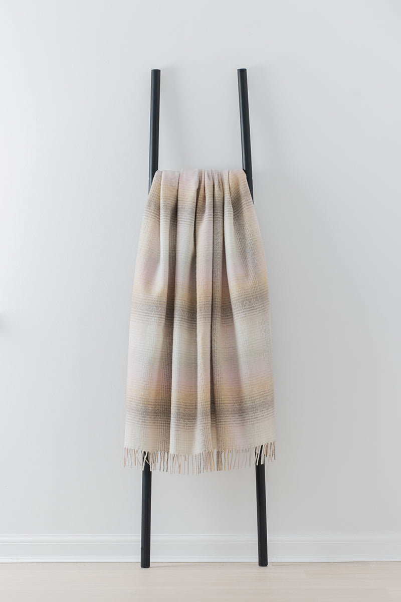 Remony lunan sands throw - Plaid blanket draped over a black metal ladder against a white background