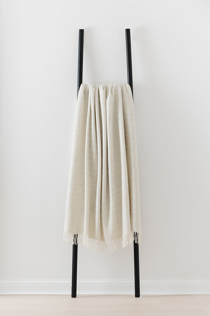 Remony lunan pebble throw - Beige towel draped over a black metal ladder against a white background