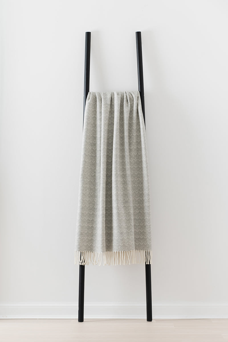 Remony lunan mist throw - Grey blanket draped over a black ladder on a white background