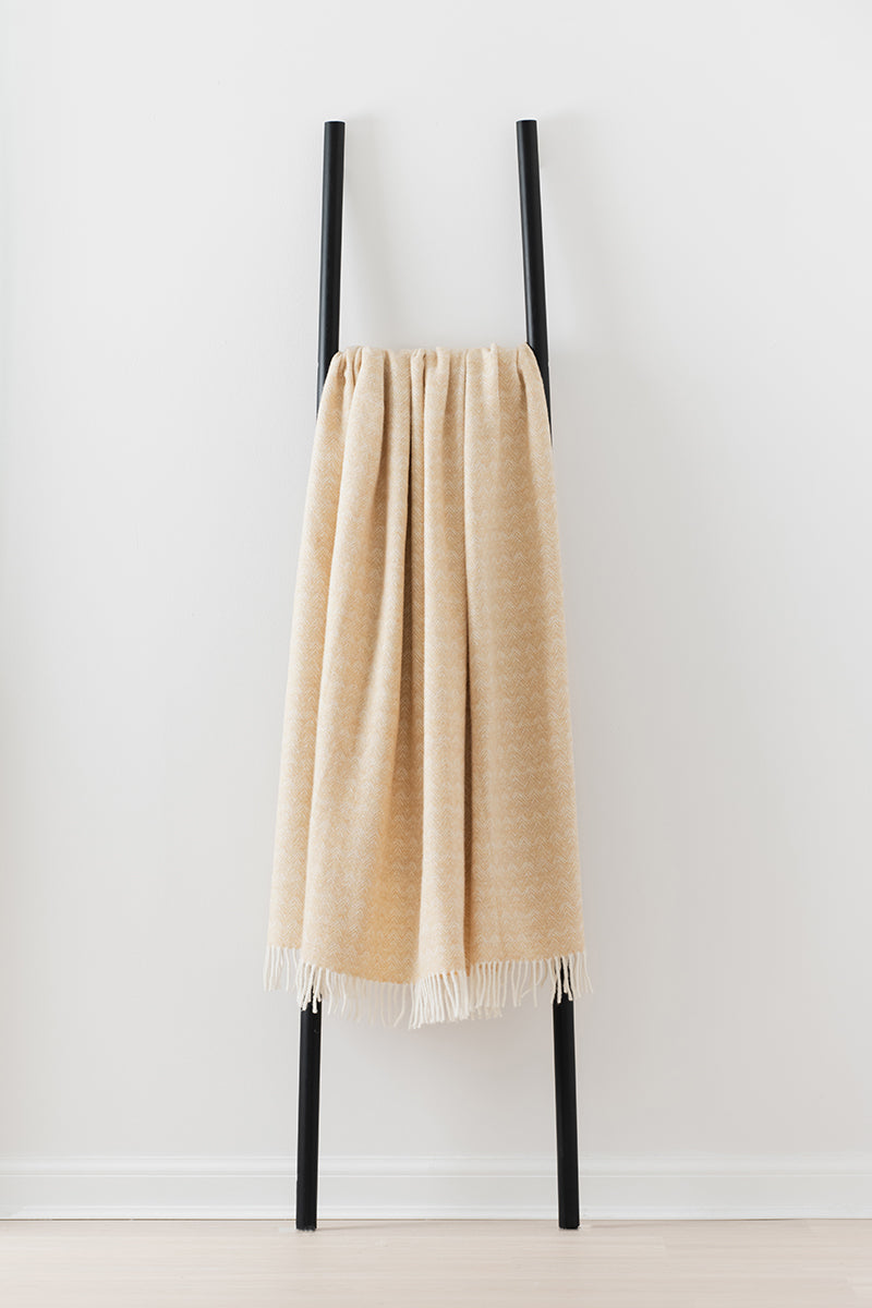 Remony lunan dune throw - Beige blanket draped over a black metal rack against a white background