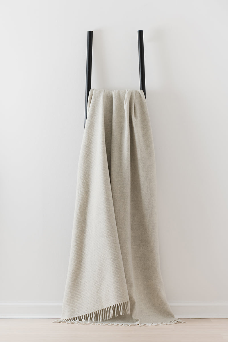 Remony clova stone, large throw - blanket with fringes draped over a black metal rack against a white wall.