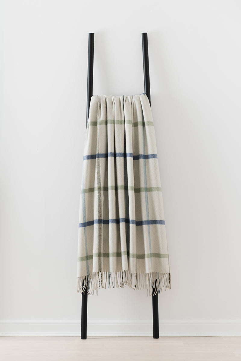 Remony milton glade throw - Plaid blanket draped over a black ladder against a white background