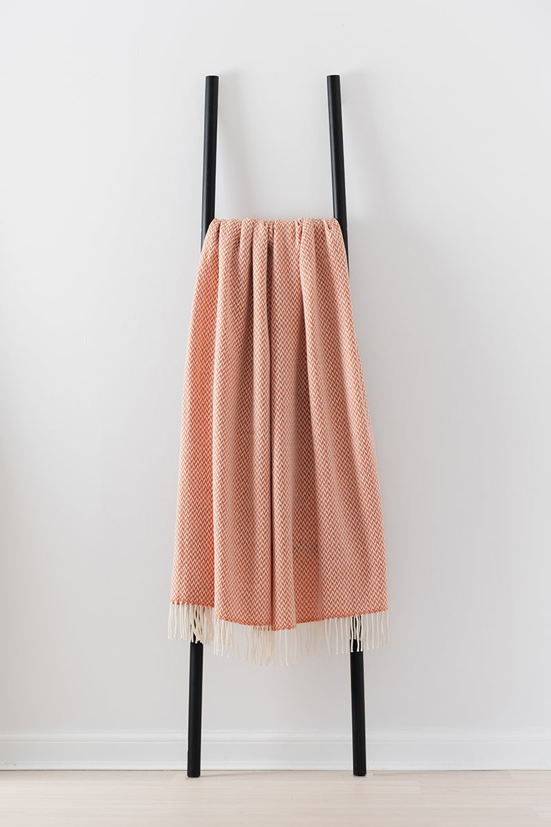 Remony balintyre clementine throw - orange textured blanket with fringe on a black stand against a white background