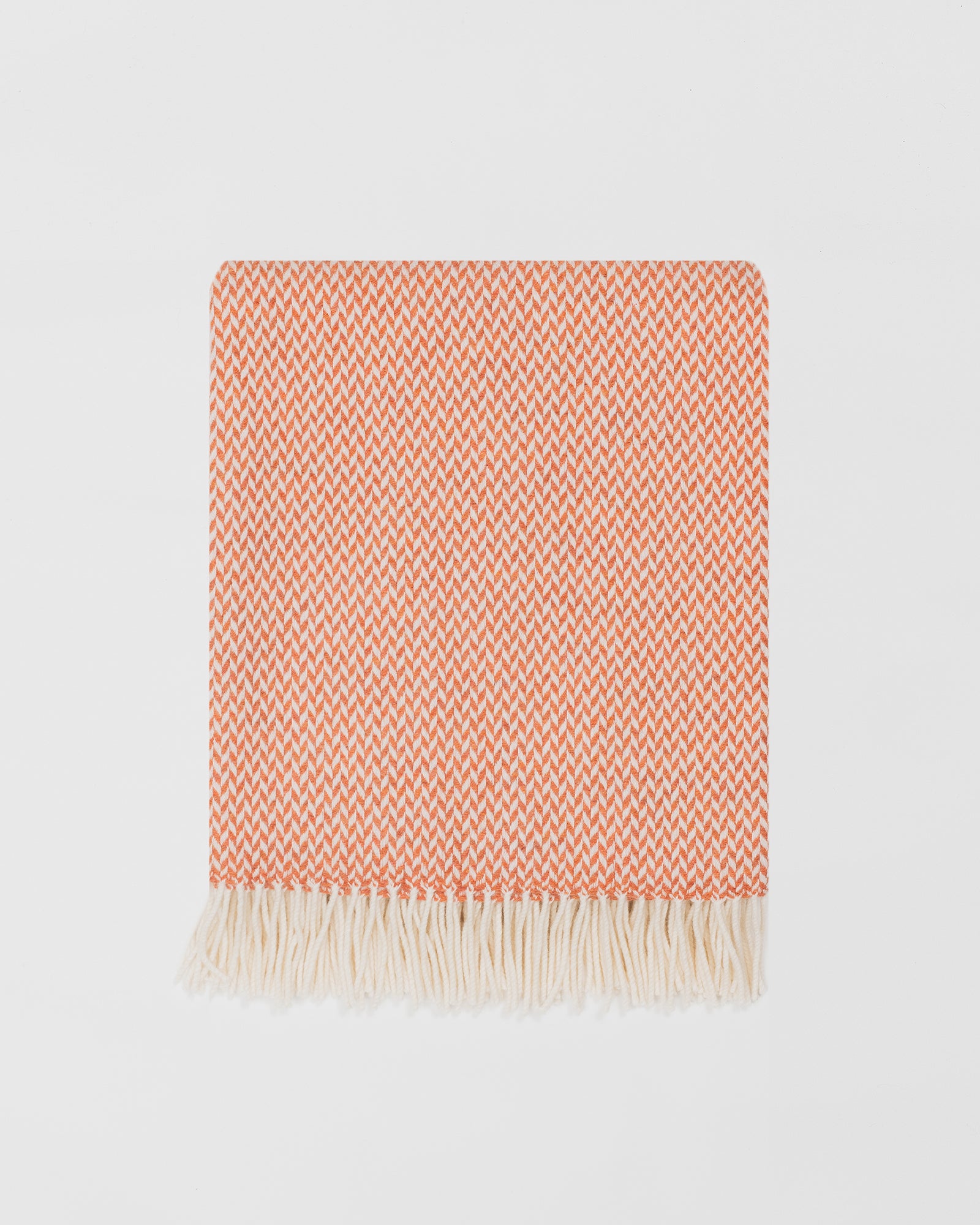 Remony balintyre clementine throw -Orange and white patterned banket with fringes on a light gray background