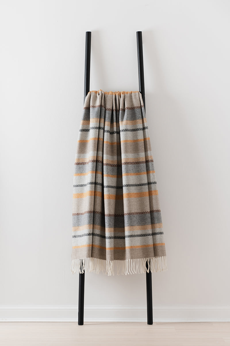 Remony croftmore amber - fair isle inspired blanket draped over a black metal ladder against a white background
