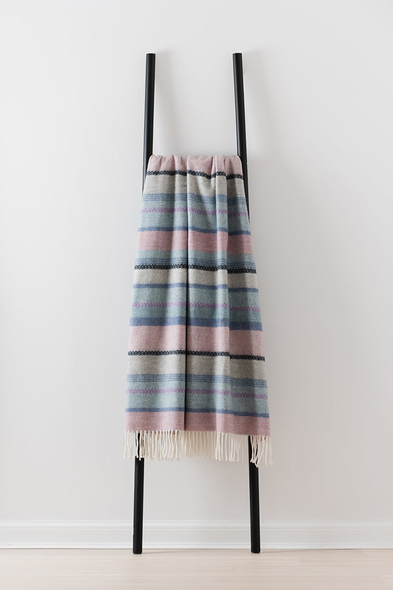 Remony croftmore heather throw - Striped blanket draped over a black ladder against a white background