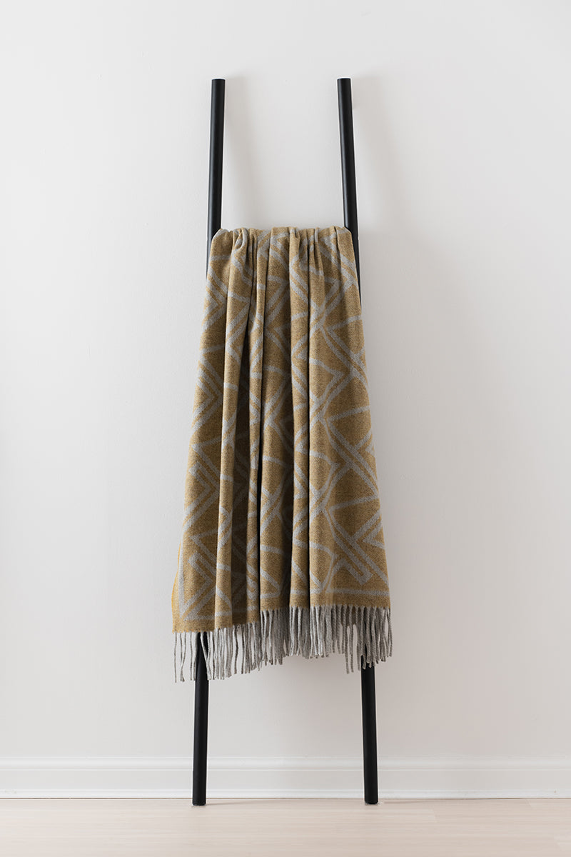 Remony fortriu mead throw - Plaid blanket with fringe draped over a black metal ladder against a white wall.