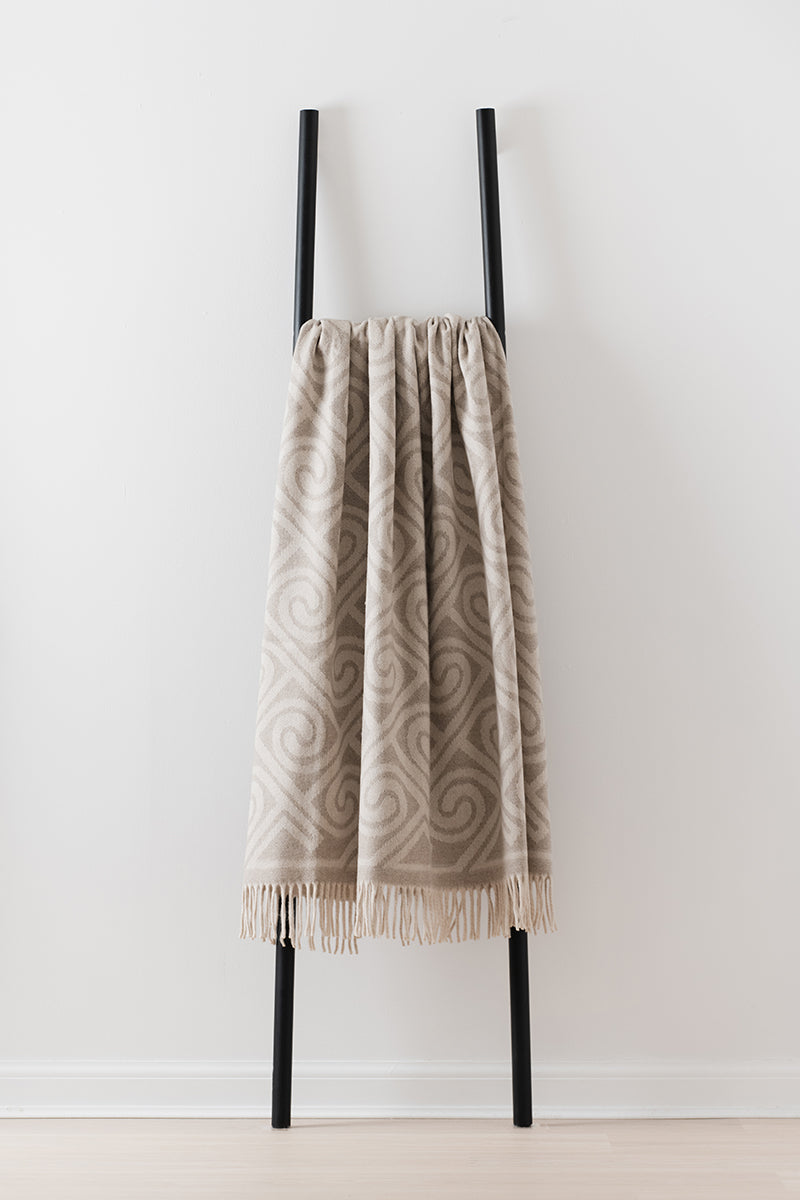 Remony fortriu stone throw - Textured blanket draped over a black metal ladder against a white wall.